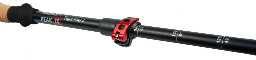 Close-up of Mons Peak IX Tiger Paw Z trekking pole showing natural cork grip, black foam extension, branded carbon shaft with height markings 49–135 cm, and red quick-lock adjustment collar

