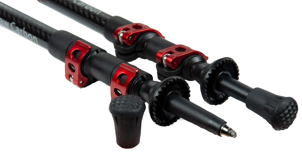 Close-up of Mons Peak IX Tiger Paw Z carbon fiber trekking poles showing black carbon weave shafts, red quick-lock collars, black foam extensions, large mud/snow baskets, and replaceable carbide tips